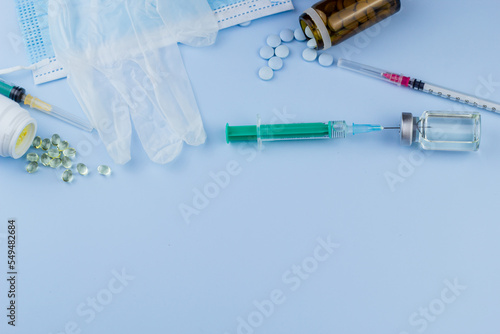 Top view of syringes, blue hygienic protective mask, gloves, tablets and glass medicine bottle ready for use. Pandemic and health concept.