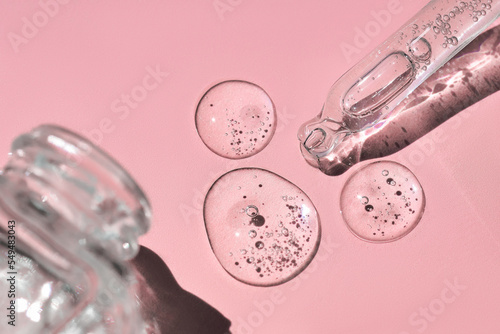 Close up of glass bottle and pipette with fluid collagen and hyaluronic acid, hydration skin with shadows on pastel pink background on sunlight. Cosmetology, dermatology concept.