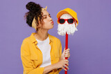 Young single fun cool happy housekeeper woman 20s wearing yellow shirt tidy up holding in hand kiss mop with hat and glasses isolated on plain pastel light purple background studio. Housework concept.