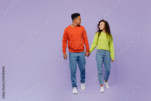 Full body young couple two friends family man woman of African American ethnicity wear casual clothes hold hands walk go together look to each other isolated on pastel plain light purple background.