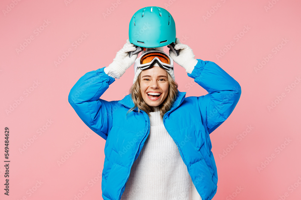 Snowboarder happy woman wears blue suit goggles mask hat padded jacket hold in hand put on ski helmet isolated on plain pastel pink background. Winter extreme sport hobby weekend trip relax concept. Snowboarder happy woman wears blue suit goggles mask hat padded jacket hold in hand put on ski helmet isolated on plain pastel pink background. Winter extreme sport hobby weekend trip relax concept.