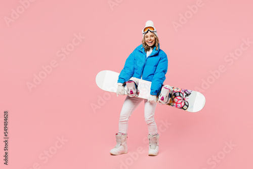 Full body snowboarder smiling fun woman wear blue suit goggles mask hat ski padded jacket hold snowboard isolated on plain pastel pink background Winter extreme sport hobby weekend trip relax concept