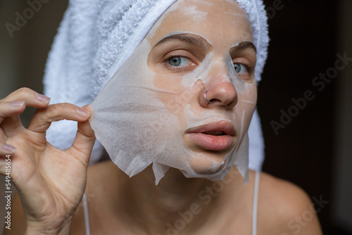 Beauty portrait woman with a towel wrapped around her head taking off sheet mask photo