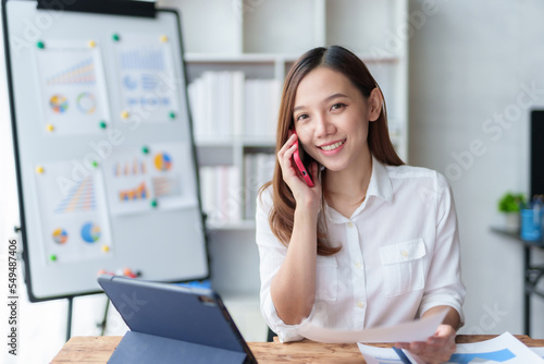 Asian businesswoman sitting happily working on a laptop and talk on the phone to contact customers, talk to explain the job and smile happily.