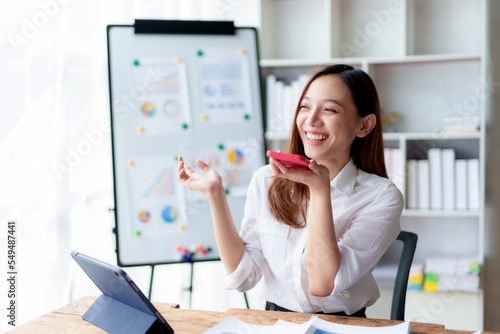 Asian businesswoman sitting happily working on a laptop and talk on the phone to contact customers, talk to explain the job and smile happily.