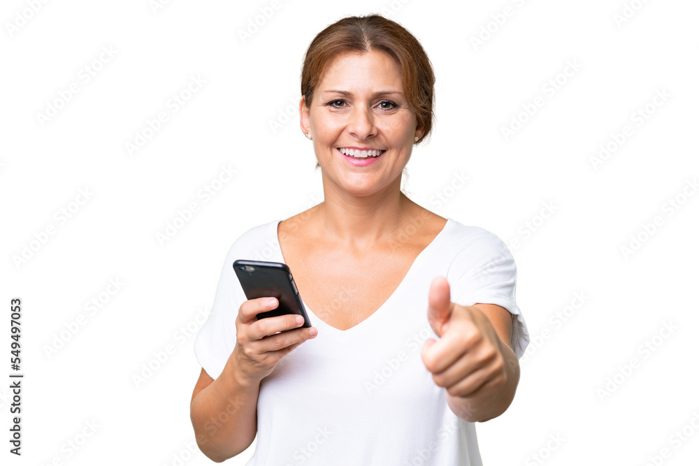 Middle-aged caucasian woman over isolated background using mobile phone while doing thumbs up Middle-aged caucasian woman over isolated background using mobile phone while doing thumbs up