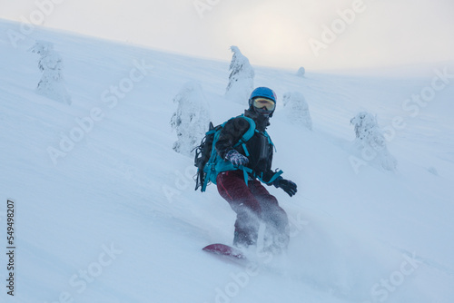 Girl on a snowboard in a snowy mountain couloir among a snow covered spruce trees