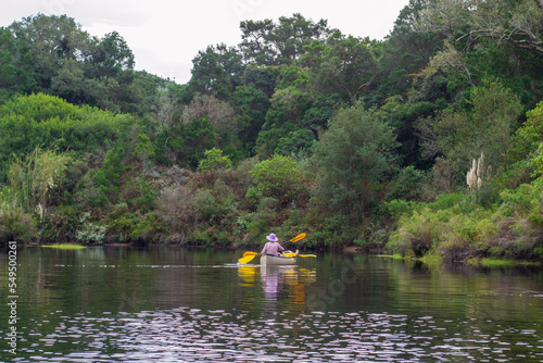 Two ladies, one young and one old taking a leisurely paddle on a river in a natural park, with trees and shrubs on the water edge