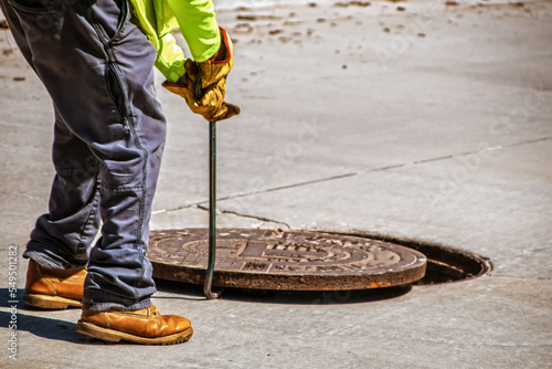 Man removing or replacing a heavy manhole cover in paved street with hook - selective focus and copy space photo