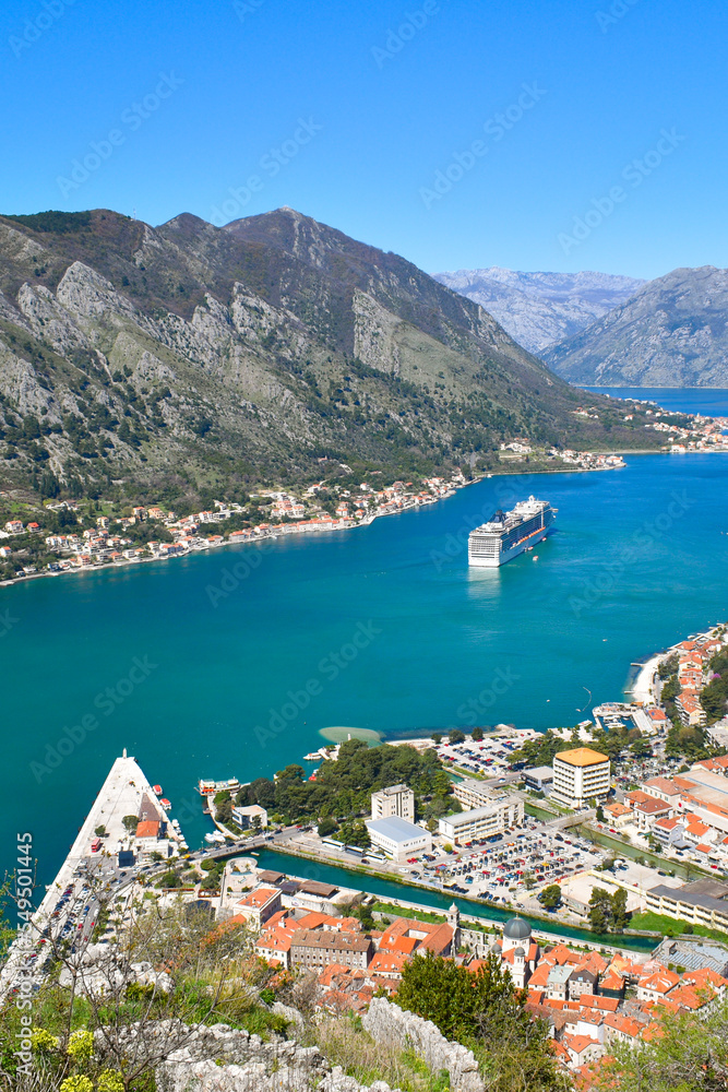 Kotor, Montenegro, Europe. Bay of Kotor on Adriatic Sea. Roofs of the buildings in the old town. Cruise in the bay, mountains in the background. Clear blue sky, sunny day.