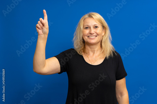 Smart proactive 40 years old woman in black t-shirt holding up index finger with great new idea isolated on blue colored background studio portrait. People lifestyle concept. photo
