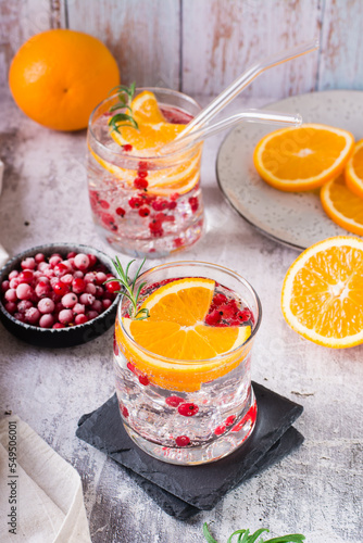 Hard seltzer cocktail with berries, orange, rosemary and ice in glasses on the table. Vertical view