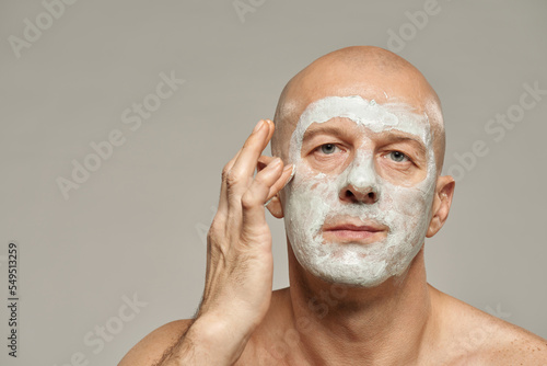 Attractive mature man applying kaolin clay mask on his face horizontal beauty portrait