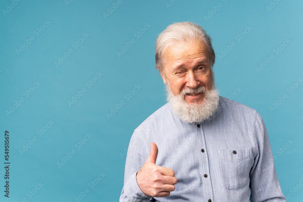 Cheerful senior bearded old man show fingers thumb up select over blue color background with copy space Cheerful senior bearded old man show fingers thumb up select over blue color background with copy space