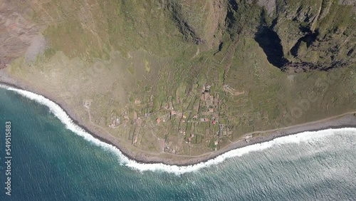 Aerial bird's eye view of an amazing cliff next to the ocean. Small village between the sea and a huge cliff. Flying upwards. Located in Madeira, Portugal.
