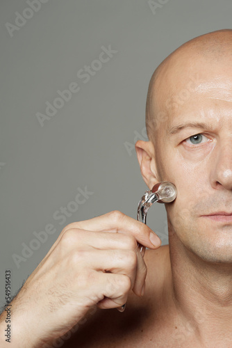 Attractive Caucasian man massaging face using microneedling beauty device studio portrait photo