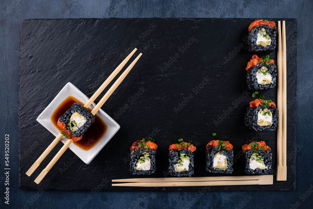 Japanese black sushi rolls with salmon, cucumber, cream cheese, soy sauce and chopsticks. Japanese black sushi rolls with salmon, cucumber, cream cheese, soy sauce and chopsticks.