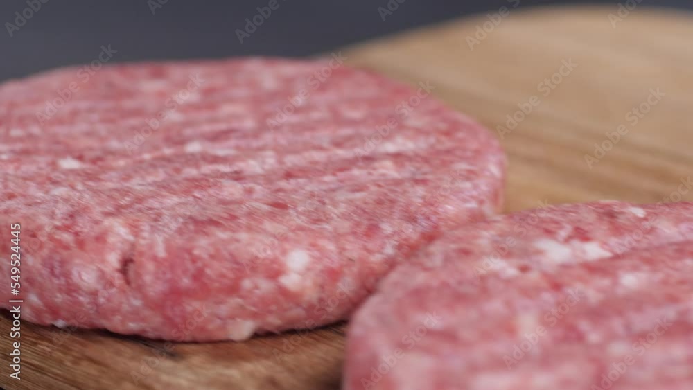Camera movement along three raw burger patties lying on a wooden board on a dark table surface background. Making hamburgers. Camera movement along three raw burger patties lying on a wooden board on a dark table surface background. Making hamburgers.