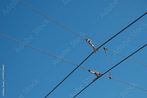 Light rail train cables cross in clear blue sky.