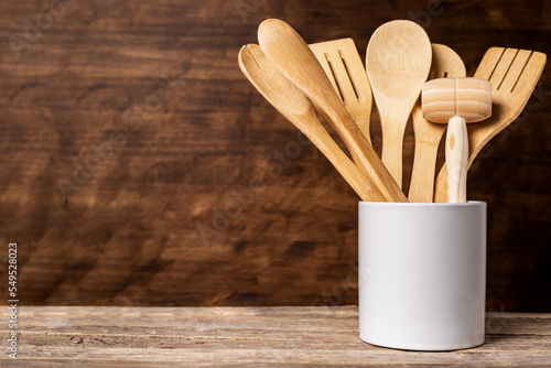 Wooden kitchen utensils inside a jar, spoon, fork, drainer and tongs among others, arranged in a decorative way with a rustic wooden background, copy space,