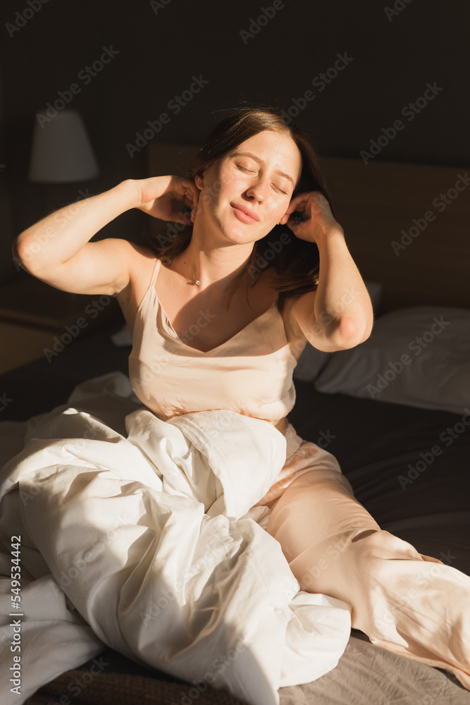 Girl portrait is waking up in morning stretches in bed and sun shines from window. Happy young woman greets new sunny day Girl portrait is waking up in morning stretches in bed and sun shines from window. Happy young woman greets new sunny day