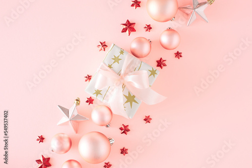 New Year concept. Flat lay photo of present box with bow pink Christmas baubles star ornaments on pastel pink background with copy space. Creative holiday card idea.