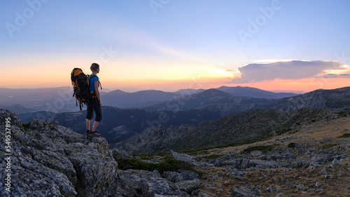 Woman hiker watching sunset on top of the mountain peak