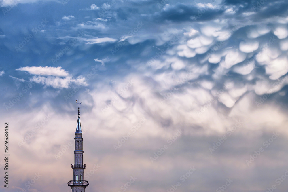 tower of Muslim mosque with crescent moon on the spire on the background of stormy epic gloomy clouds tower of Muslim mosque with crescent moon on the spire on the background of stormy epic gloomy clouds