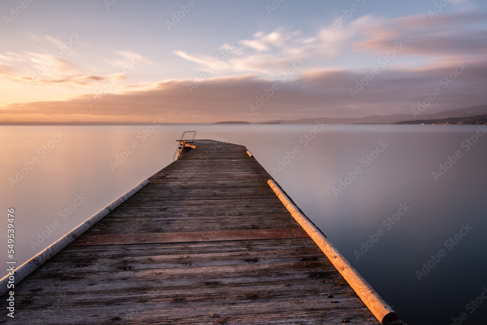 Long exposure view of a pier on a lake at sunset, with perfectly still water