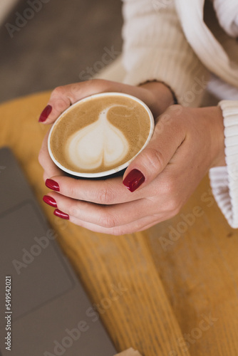 Pictures of women's hands holding a paper cup of coffee. Coffee to go concept. Top view of laptop computer. Freelance work.