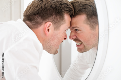 Caucasian man being angry on himself screaming on his reflection on the mirror