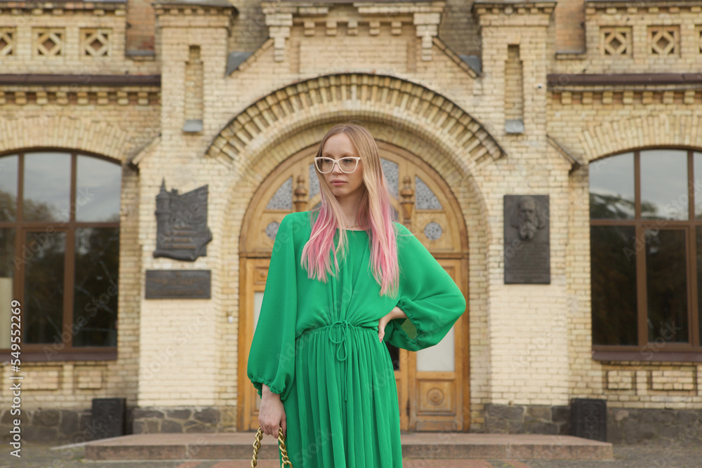 Stylish pink haired woman wearing green dress, standing in front of an old beautiful building