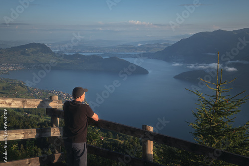 A man on a viewpoint at the top of a mountain looks out over a magnificent landscape of a lake surrounded by mountains. Lake Lucerne  Vierwaldstattersee. Swiss Alps  Switzerland