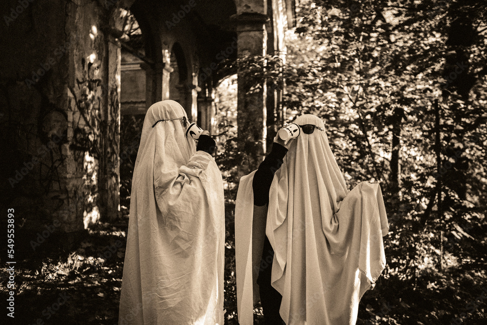 Naklejka premium A funny image of two people in ghost costumes and sunglasses holding a cup with a drink in an abandoned building, black and white image