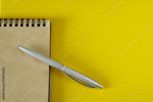 A spring-loaded notepad made from eco-friendly recycled paper and a silver fountain pen lie on a yellow textured anti-stress surface. Copy space.
