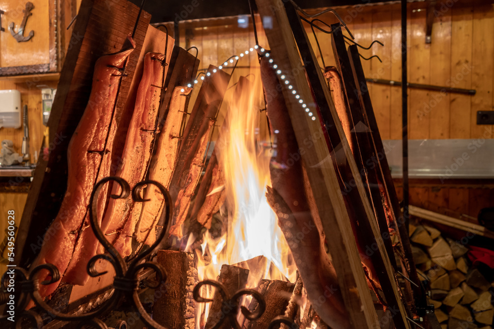 Selective focus and night view of burning fire and hanging grilled salmon at stall in Christmas market in Germany. 