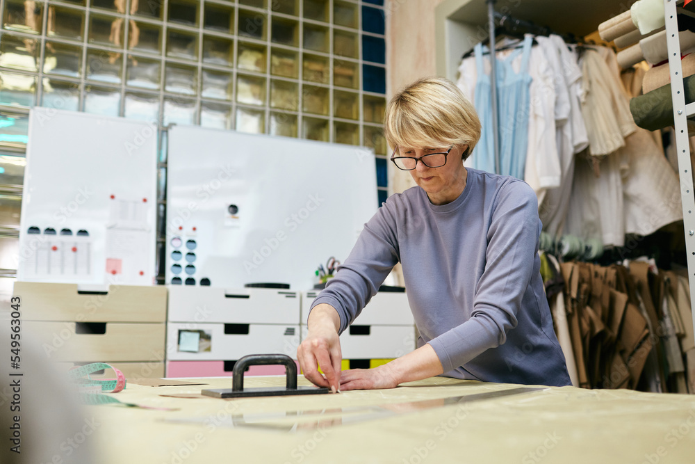 Mature Caucasian woman working in tailor workshop transferring pattern onto fabric Mature Caucasian woman working in tailor workshop transferring pattern onto fabric
