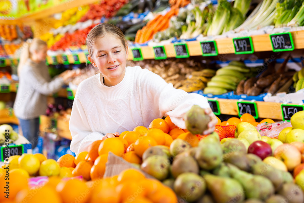 Happy smiling teenage girl making purchases in supermarket, choosing fresh ripe fruits
