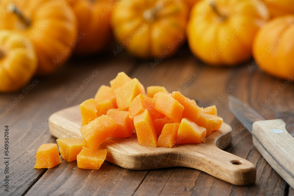Chopped pumpkin pulp on a cutting board. Several pumpkins in background. Chopped pumpkin pulp on a cutting board. Several pumpkins in background.