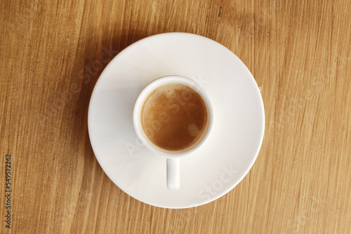 Top view of white porcelain cup with plate of hot coffee with milk on wooden table background.