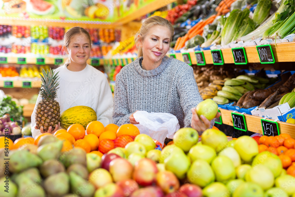 Mom and her teen daughter pick pineapple and melon at the grocery supermarket