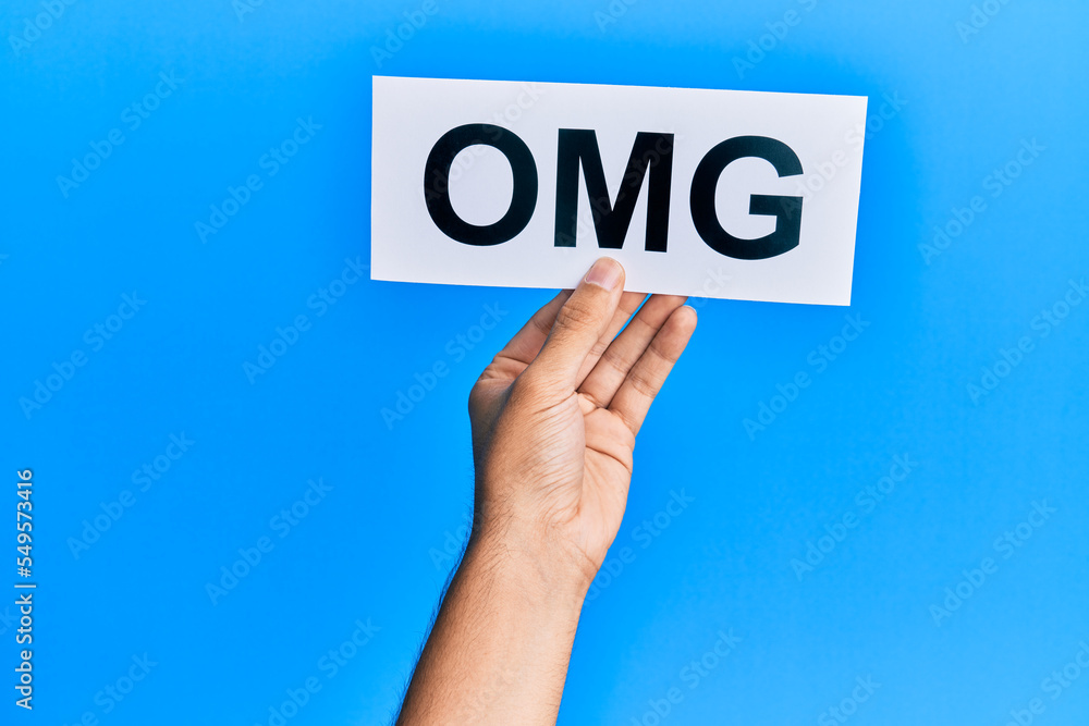 Hand of caucasian man holding paper with omg word over isolated blue background Hand of caucasian man holding paper with omg word over isolated blue background