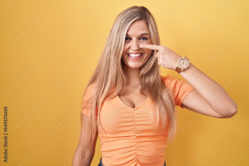 Young woman standing over yellow background pointing with hand finger to face and nose, smiling cheerful. beauty concept Young woman standing over yellow background pointing with hand finger to face and nose, smiling cheerful. beauty concept