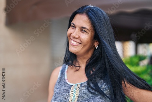 Middle age hispanic woman smiling confident looking to the side at street