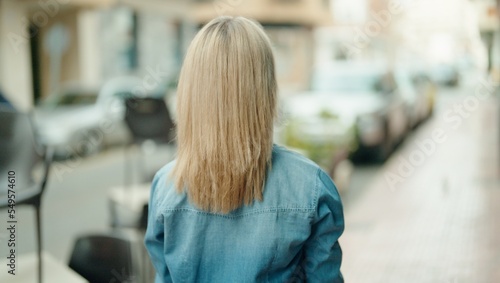 Young blonde woman standing on back view at street