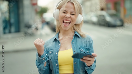 Young blonde woman smiling confident playing video game at street