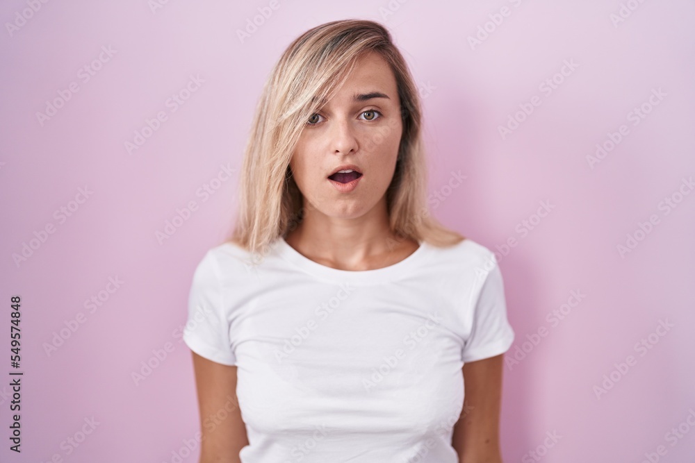Young blonde woman standing over pink background afraid and shocked with surprise and amazed expression, fear and excited face. Young blonde woman standing over pink background afraid and shocked with surprise and amazed expression, fear and excited face.