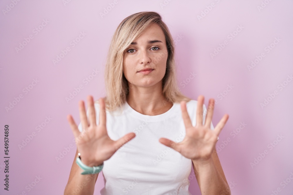 Fototapeta premium Young blonde woman standing over pink background moving away hands palms showing refusal and denial with afraid and disgusting expression. stop and forbidden.