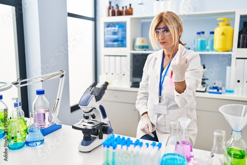 Middle age blonde woman working at scientist laboratory showing middle finger  impolite and rude fuck off expression