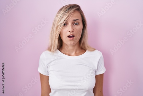 Young blonde woman standing over pink background afraid and shocked with surprise and amazed expression, fear and excited face.